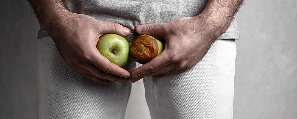 Beide Hände von einem Mann halten jeweils einen Apfel vor dem Intimbereich. Der rechte Apfel ist vergammelt - Krebsfrüherkennung - Urologie, Mannheim